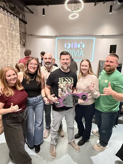 Group of six people smiling and posing with a trophy at a trivia event.